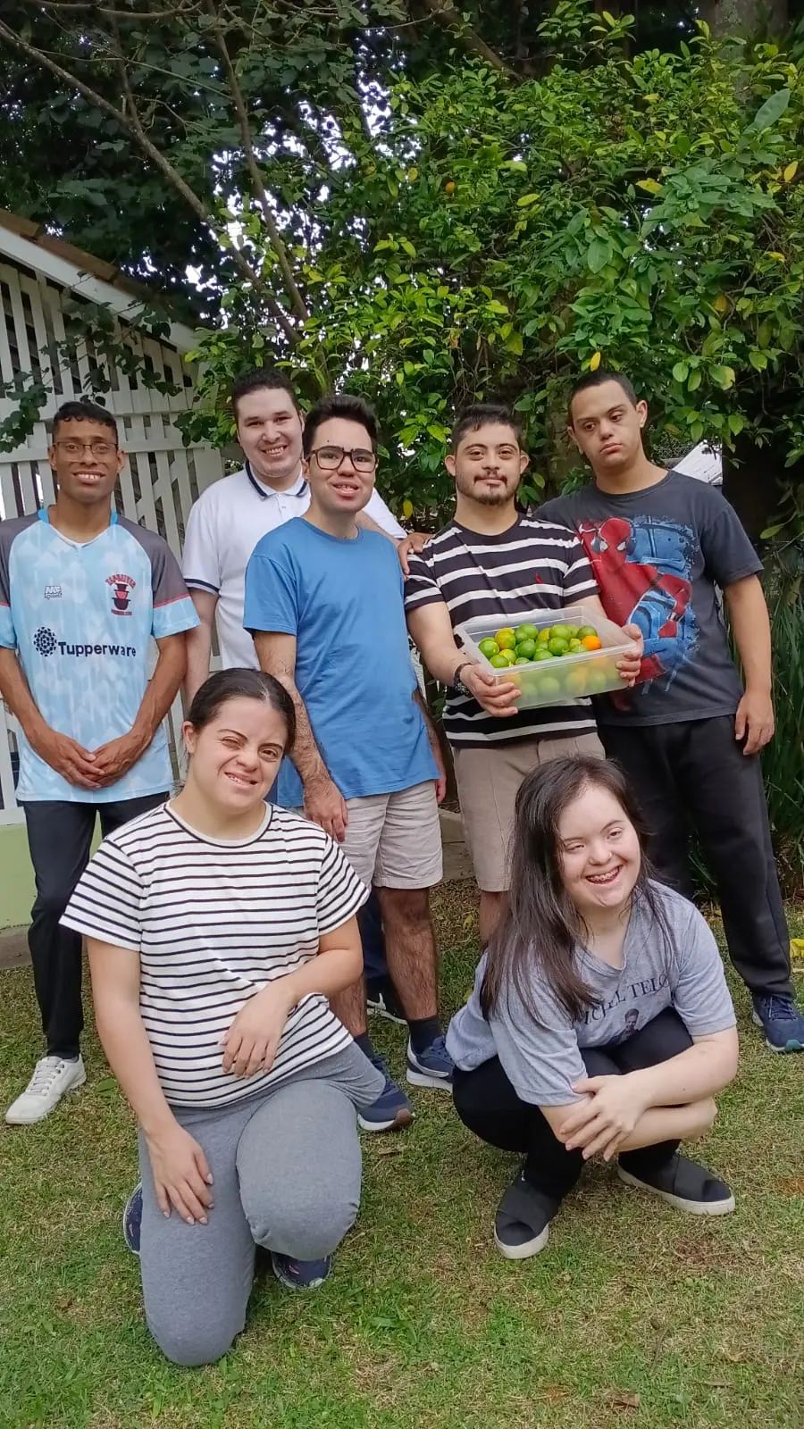 Grupo de adultos atendidos pela Fundação posando juntos no jardim com uma caixa de limões